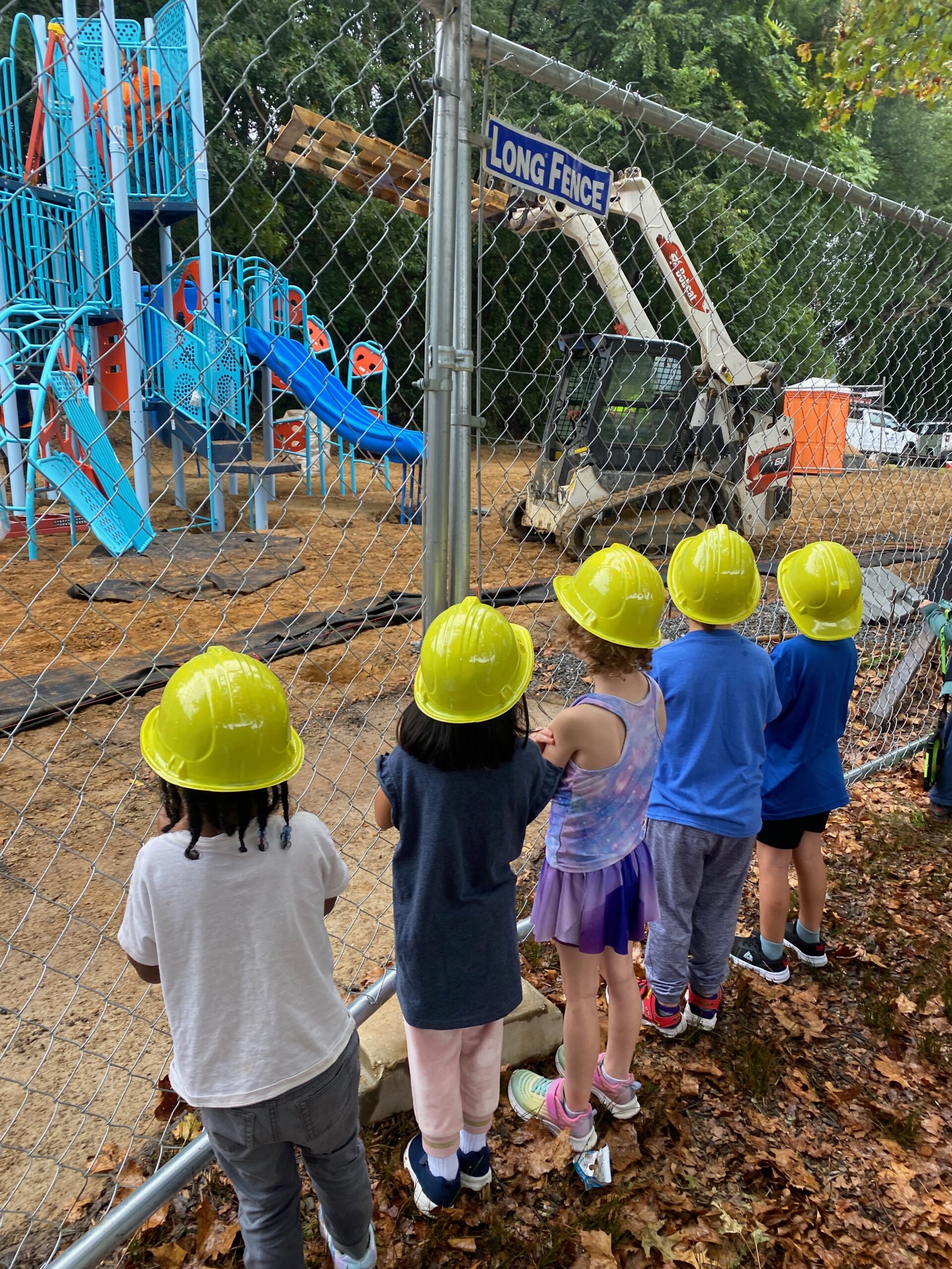 Students in yellow hard hats watched as the playground gets built